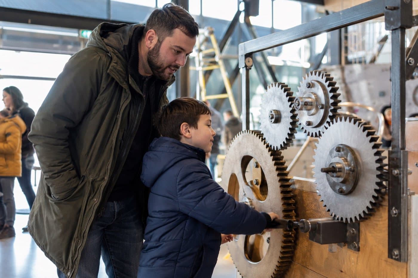 Отец и сын рассматривают шестерёнчатый механизм в интерактивном музее